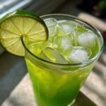 Close-up of a tall glass filled with bright green Easy Iced Cucumber Lime Agua Fresca and ice, garnished with a lime wheel.