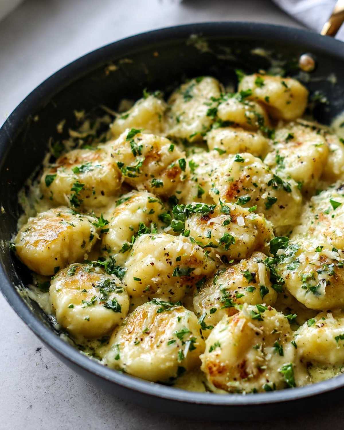 Close-up of pan-seared gnocchi coated in a creamy garlic butter sauce, topped with fresh parsley.