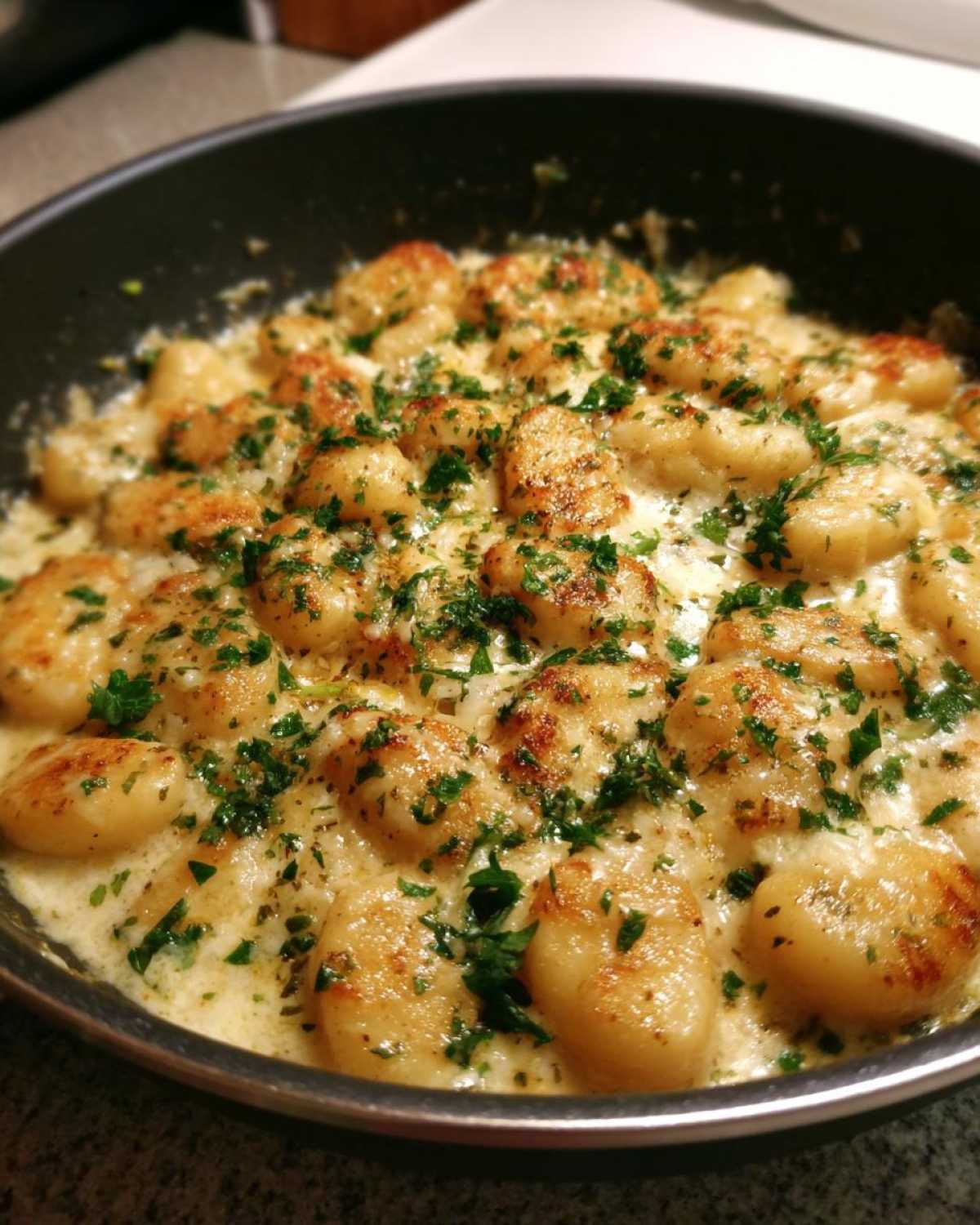 Close-up of golden pan-seared gnocchi swimming in a creamy garlic butter sauce, topped with fresh parsley.