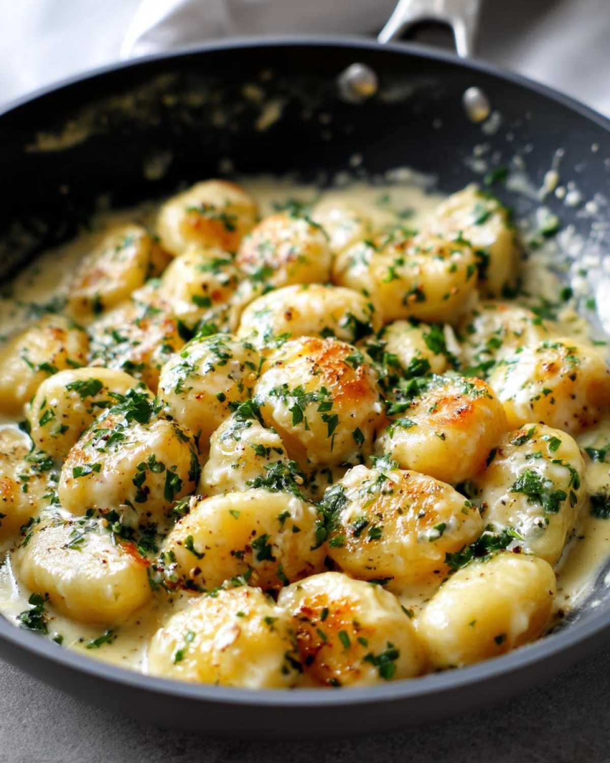 Close-up of golden pan-seared gnocchi coated in a creamy garlic butter sauce and topped with fresh parsley.