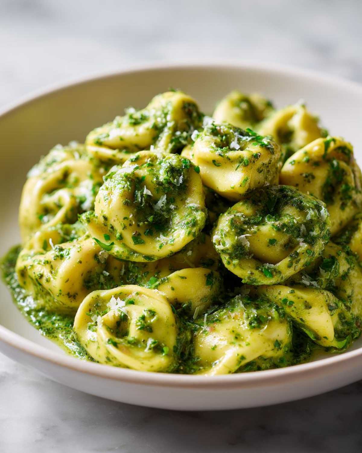 A close-up of a bowl filled with Easy One-Pot Creamy Pesto Tortellini, coated in vibrant green pesto sauce and topped with grated cheese.