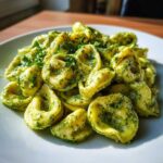 A close-up, appetizing photo of Easy One-Pot Creamy Pesto Tortellini coated in vibrant green pesto sauce and garnished with fresh parsley.