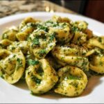 Close-up of Easy One-Pot Creamy Pesto Tortellini tossed in vibrant green pesto sauce and topped with grated cheese.