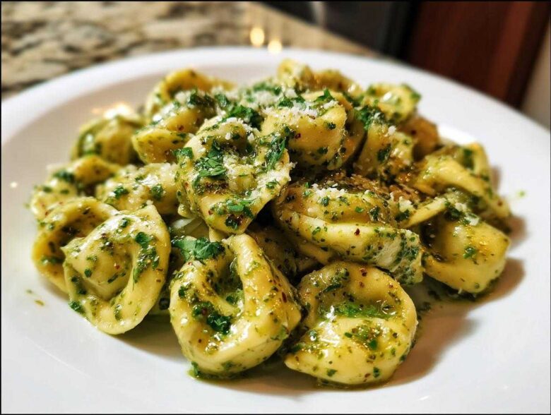 Close-up of Easy One-Pot Creamy Pesto Tortellini tossed in vibrant green pesto sauce and topped with grated cheese.