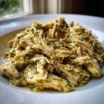 Close-up of shredded chicken coated in a creamy, green salsa verde sauce, ready to serve.
