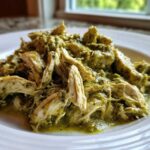 Close-up of shredded chicken coated in a rich, creamy salsa verde sauce served on a white plate.
