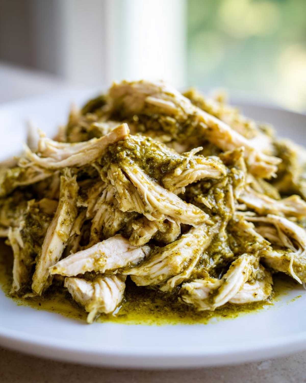 Close-up of shredded chicken coated in a vibrant green, creamy salsa verde sauce, ready to serve.