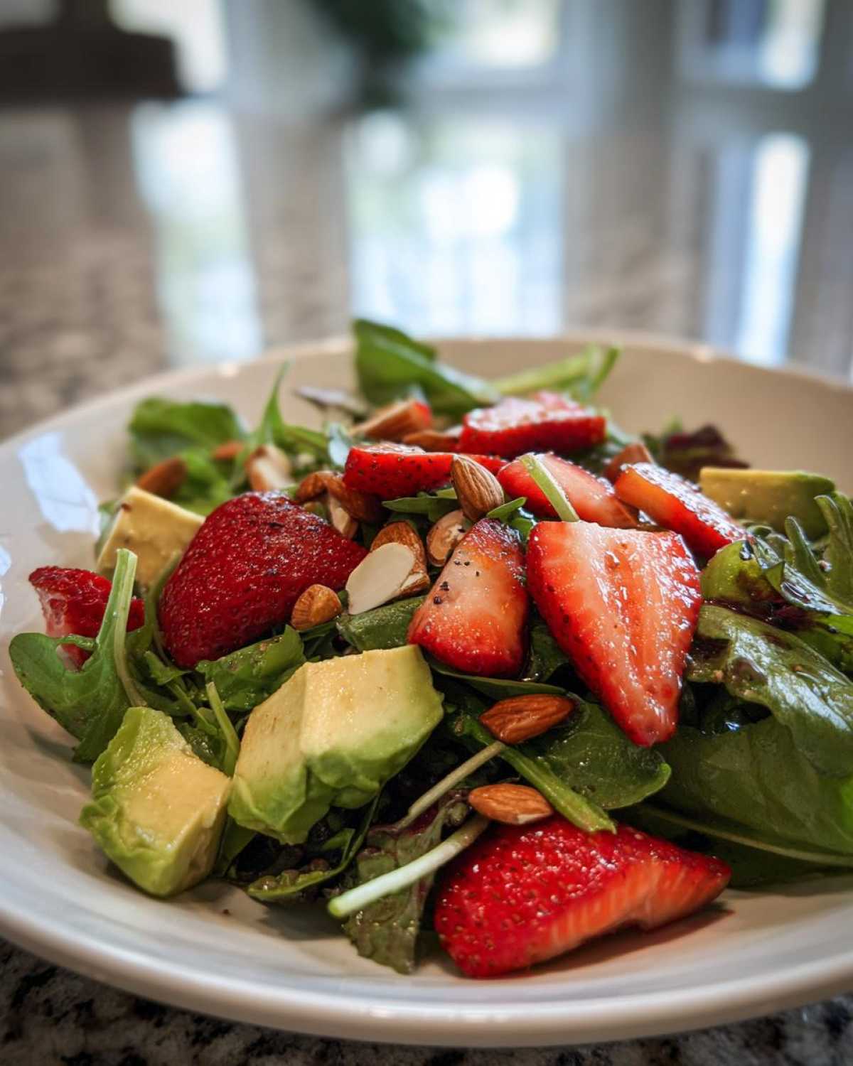 A close-up of an Easy Strawberry Avocado Salad featuring mixed greens, sliced strawberries, avocado chunks, and slivered almonds.