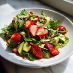 Close-up of a vibrant Easy Strawberry Avocado Salad featuring fresh greens, sliced strawberries, avocado chunks, and slivered nuts.
