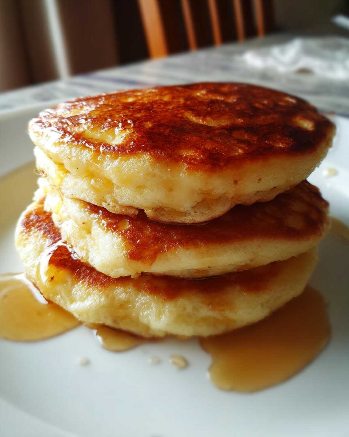 Close-up of a tall stack of three fluffy Banana Pancakes, golden brown and dripping with syrup on a white plate.