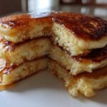 Close-up of a tall stack of fluffy Banana Pancakes cut to show the airy interior, drizzled with golden syrup.