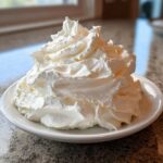 A large dollop of fluffy, white whipped topping served on a small white plate, suggesting a component of Cream Cheese Frosting.