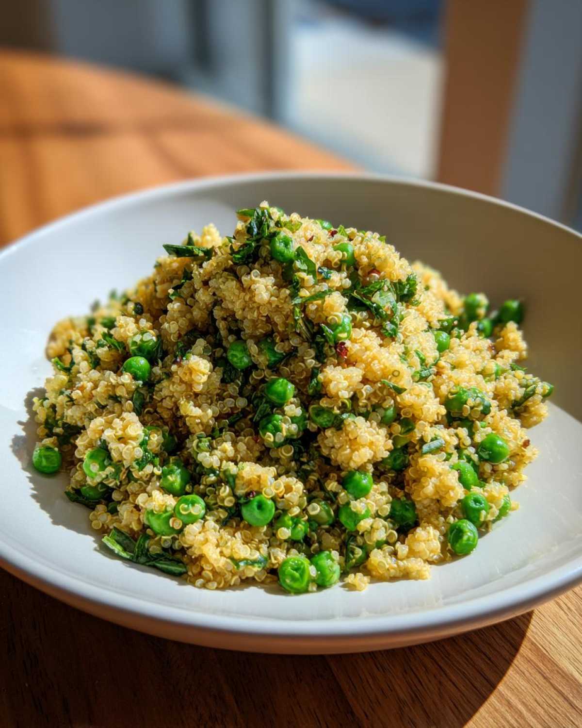 A close-up of fluffy Garlic Butter Quinoa Green Peas mixed with fresh herbs in a light-colored bowl.