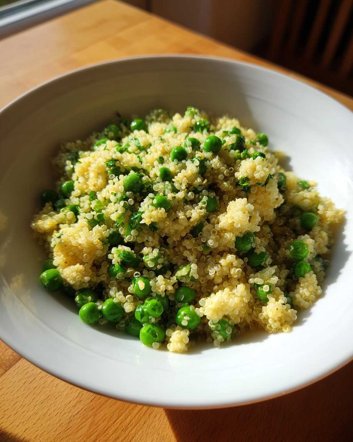 A close-up of bright Garlic Butter Quinoa Green Peas served in a white bowl on a wooden surface.