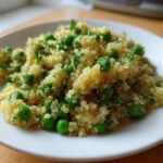 Close-up of fluffy Garlic Butter Quinoa Green Peas mixed with bright green peas and herbs on a white plate.