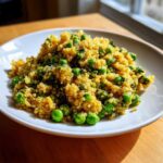 A close-up of Garlic Butter Quinoa Green Peas served on a white plate, brightly lit by natural light.