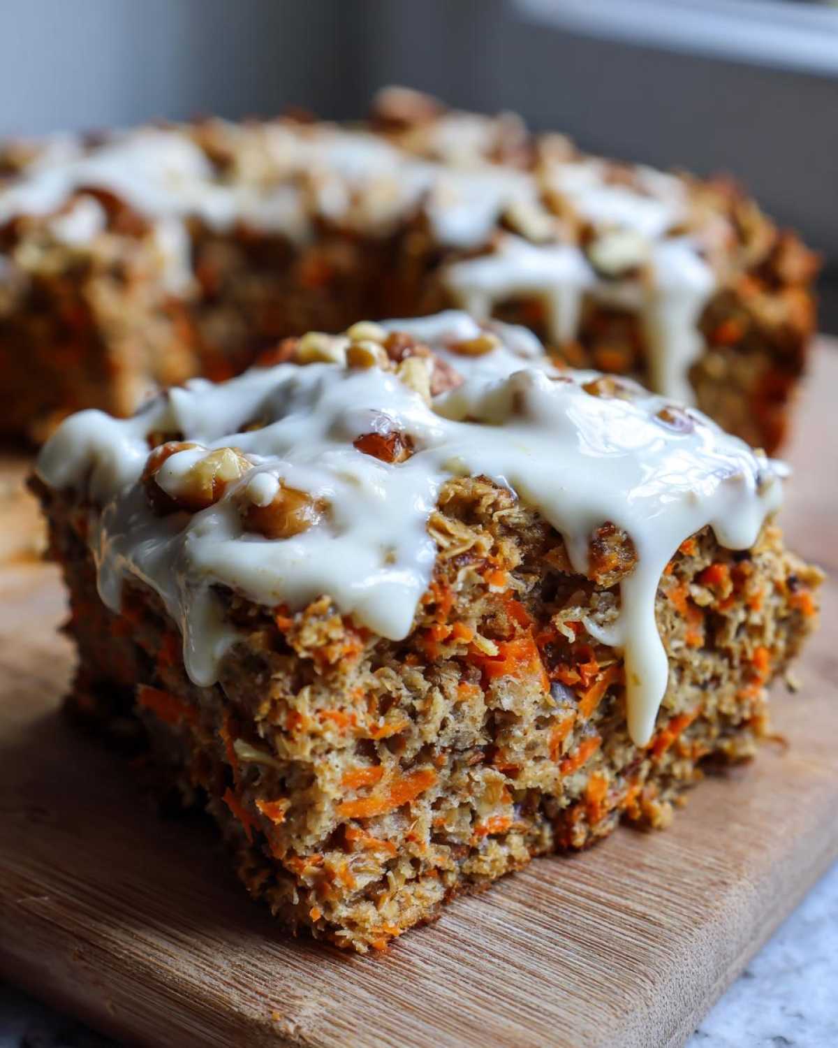 Close-up of a slice of Gluten-Free Carrot Cake Baked Oats topped with white frosting and chopped walnuts.