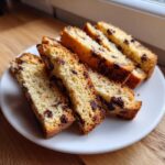 Close-up of several slices of golden-brown Gluten-Free Chocolate Chip Biscotti arranged on a white plate.