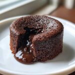 Close-up of a single Gluten-Free Chocolate Lava Brownie Cup with molten chocolate oozing out onto a white plate.