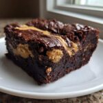 A close-up of a rich, fudgy Gluten-Free Chocolate Peanut Butter Swirl Brownies square on a white plate.