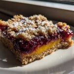 A single serving of Gluten-Free Lemon Berry Crumble Bars with a bright yellow lemon layer and dark berry topping, dusted with powdered sugar.