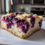 A close-up of a single square of Gluten-Free Lemon Blueberry Cheesecake Squares on a white plate.