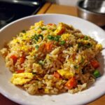 Close-up of a bowl filled with Gluten-Free Lemon Pepper Fried Rice, featuring scrambled egg, carrots, and lemon zest.