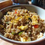Close-up of a bowl filled with Gluten-Free Lemon Pepper Fried Rice, featuring scrambled egg pieces and bright yellow lemon zest.