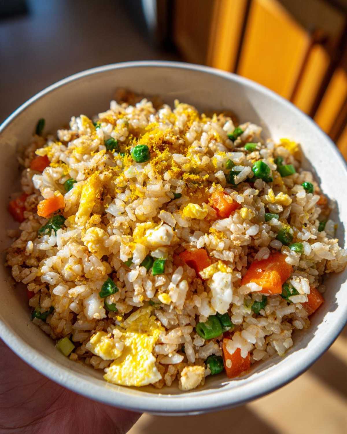Close-up of a bowl of Gluten-Free Lemon Pepper Fried Rice mixed with scrambled egg, carrots, and peas, topped with zest.