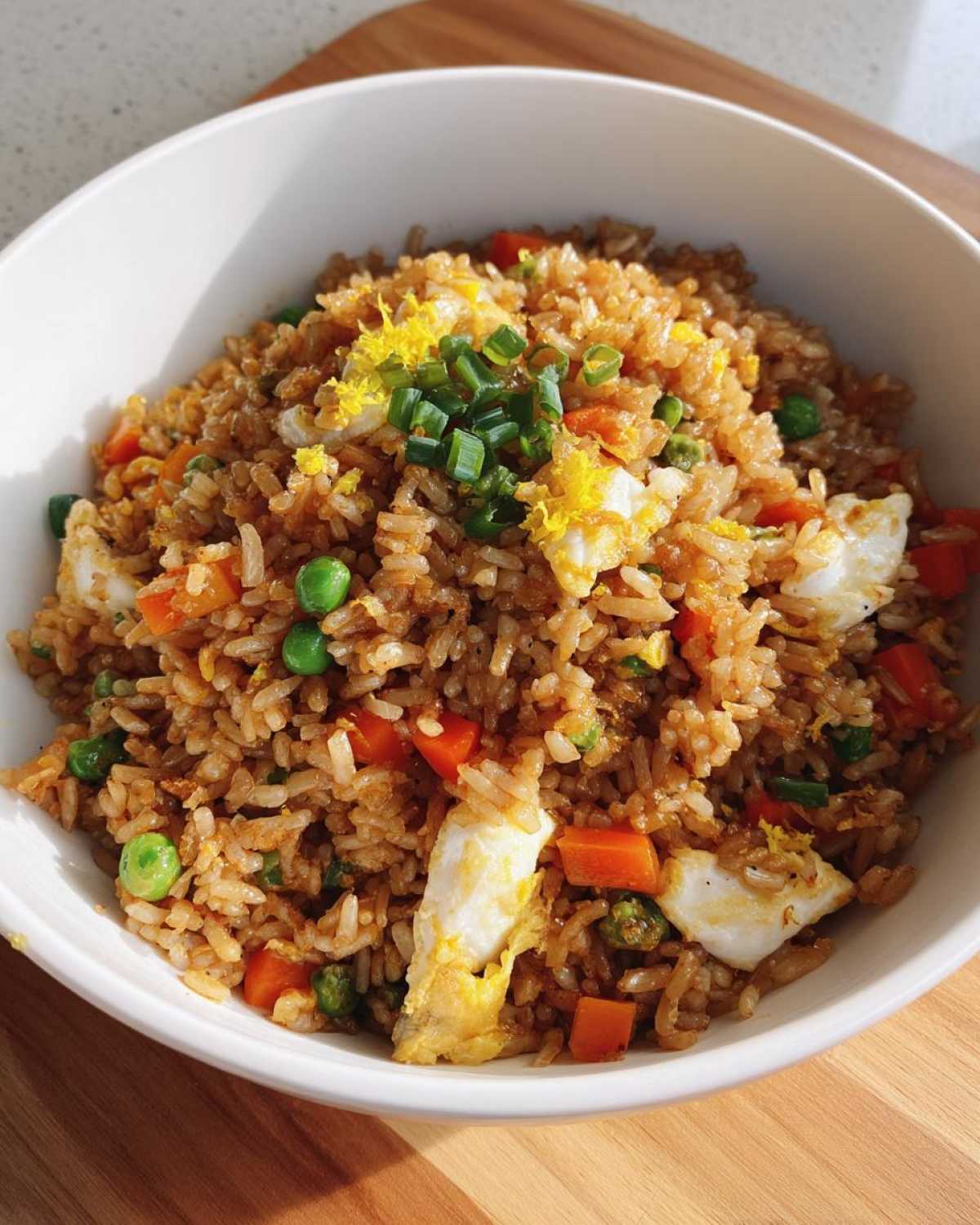 A close-up of Gluten-Free Lemon Pepper Fried Rice mixed with scrambled egg pieces, peas, and carrots, topped with green onions.