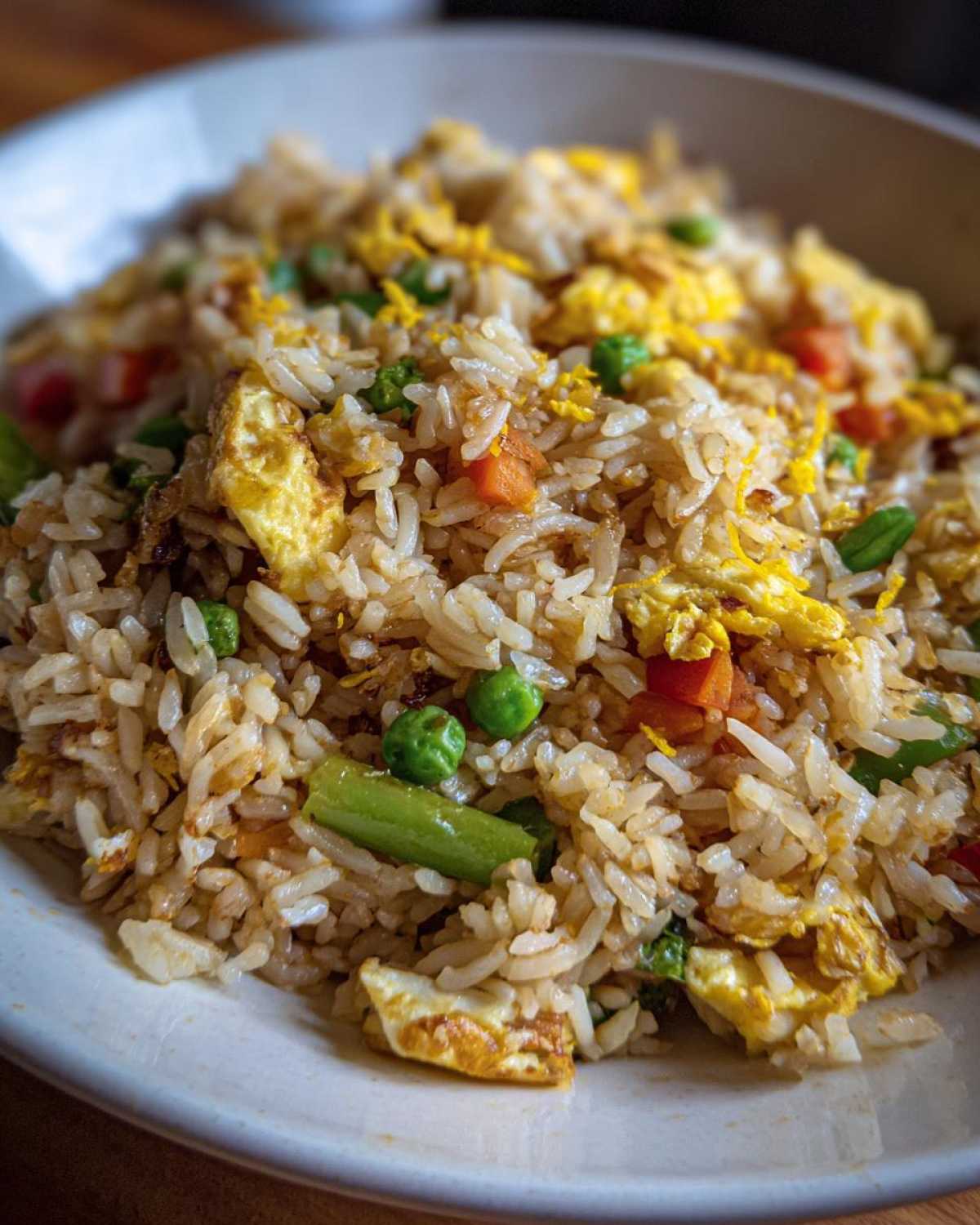 Close-up of a bowl filled with flavorful Gluten-Free Lemon Pepper Fried Rice mixed with scrambled egg, peas, and carrots.