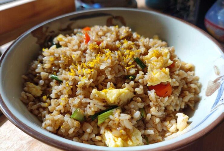 Close-up of a bowl filled with Gluten-Free Lemon Pepper Fried Rice, featuring scrambled egg pieces and bright yellow lemon zest.