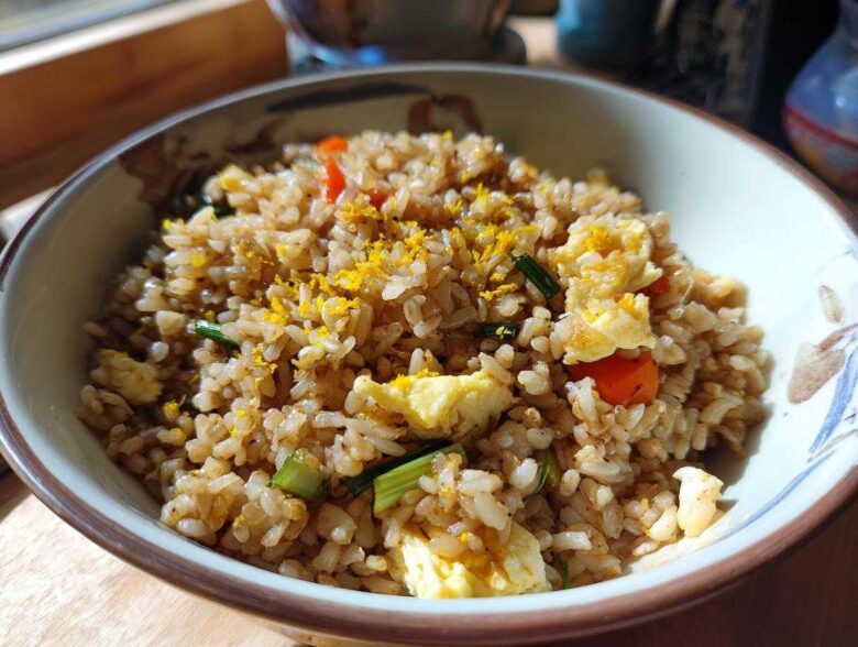 Close-up of a bowl filled with Gluten-Free Lemon Pepper Fried Rice, featuring scrambled egg pieces and bright yellow lemon zest.