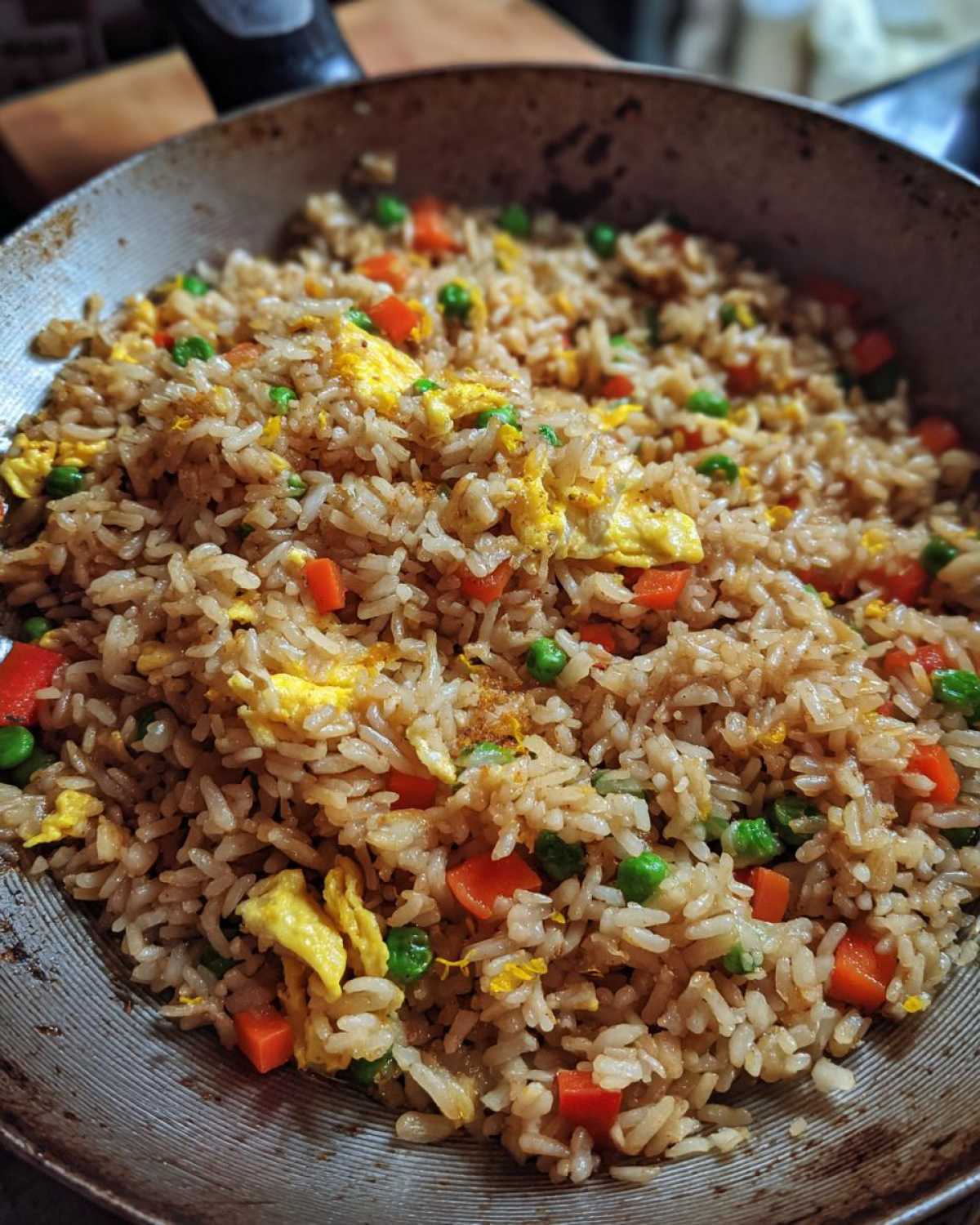 Close-up of freshly cooked Gluten-Free Lemon Pepper Fried Rice with scrambled egg, carrots, and peas in a wok.