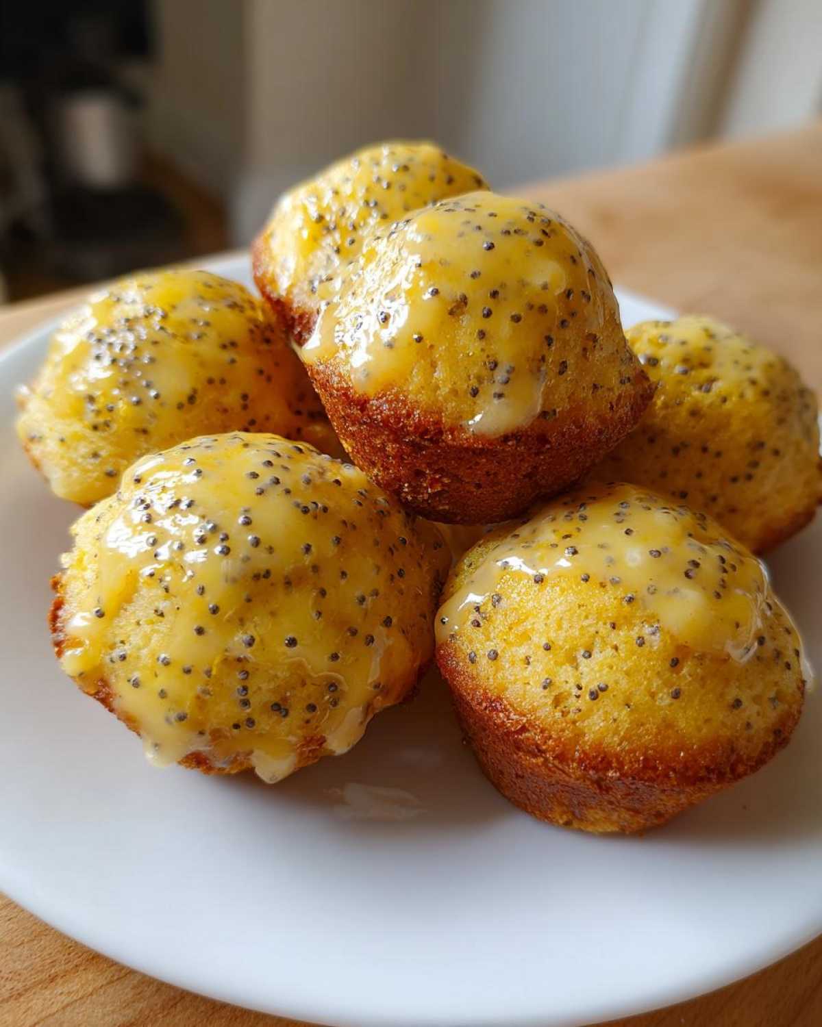 A stack of freshly baked Gluten-Free Lemon Poppy Seed Donut Holes drizzled with a bright yellow lemon glaze and poppy seeds.
