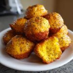 A stack of bright yellow Gluten-Free Lemon Poppy Seed Donut Holes topped with poppy seeds on a white plate.