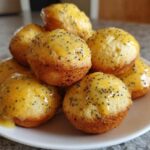 A stack of freshly baked Gluten-Free Lemon Poppy Seed Donut Holes topped with a bright yellow lemon glaze and poppy seeds.