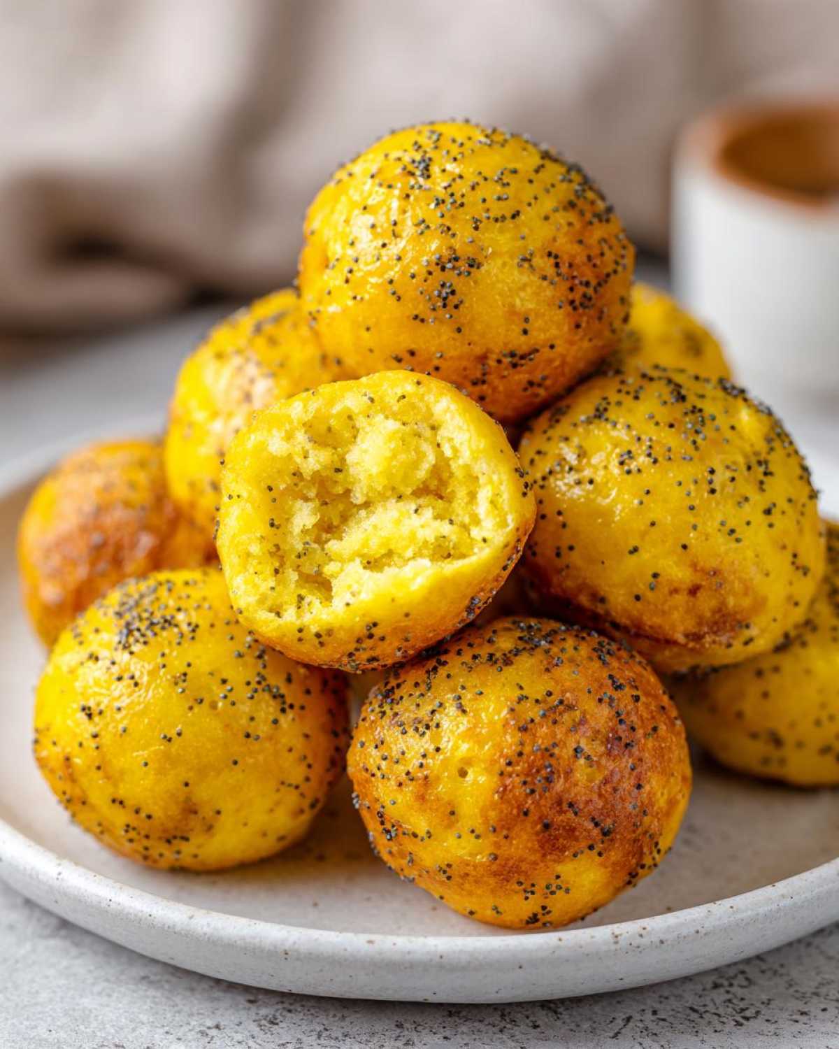 A stack of bright yellow Gluten-Free Lemon Poppy Seed Donut Holes, one cut open to show the fluffy interior.
