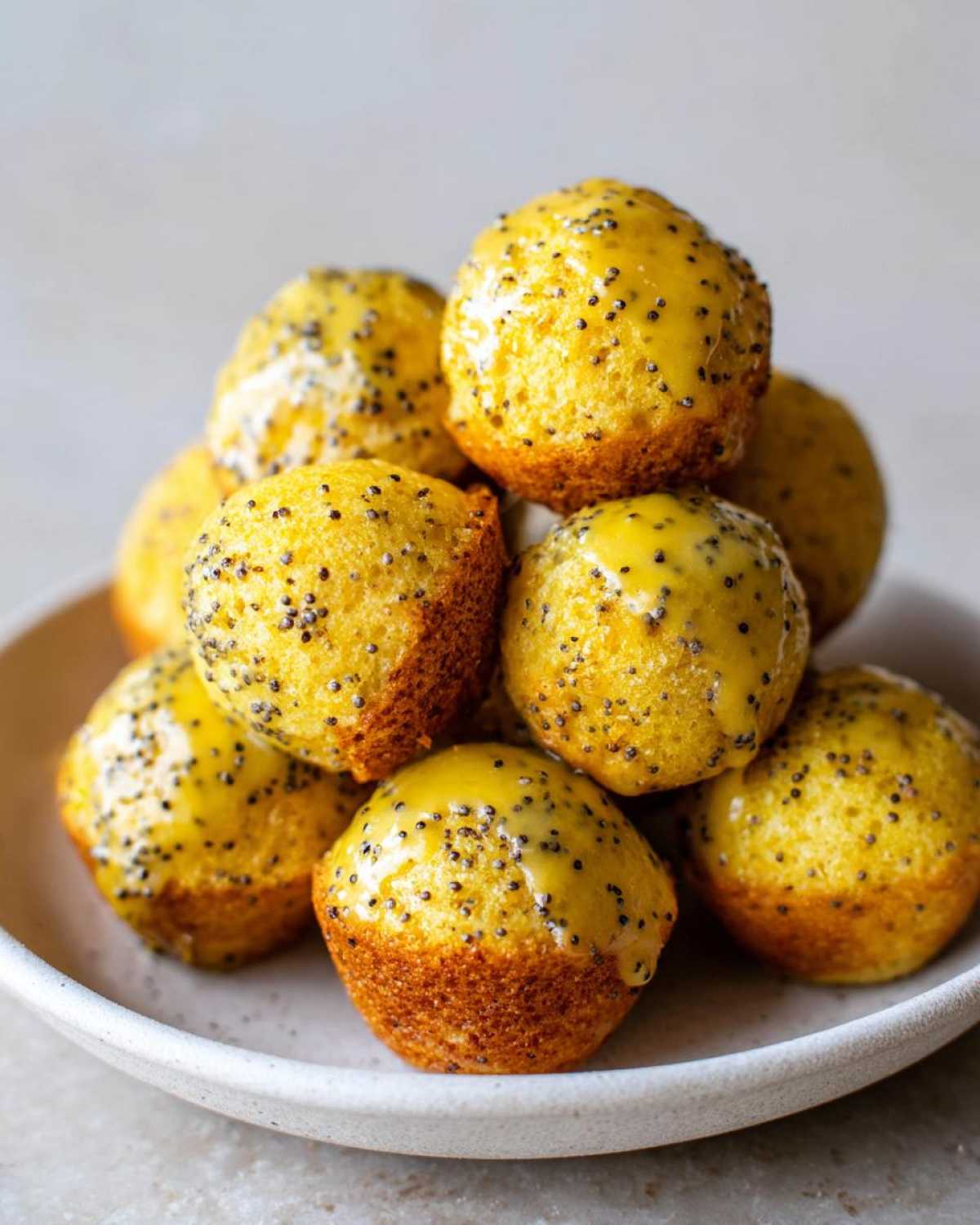 A stack of bright yellow Gluten-Free Lemon Poppy Seed Donut Holes topped with a shiny lemon glaze and poppy seeds.