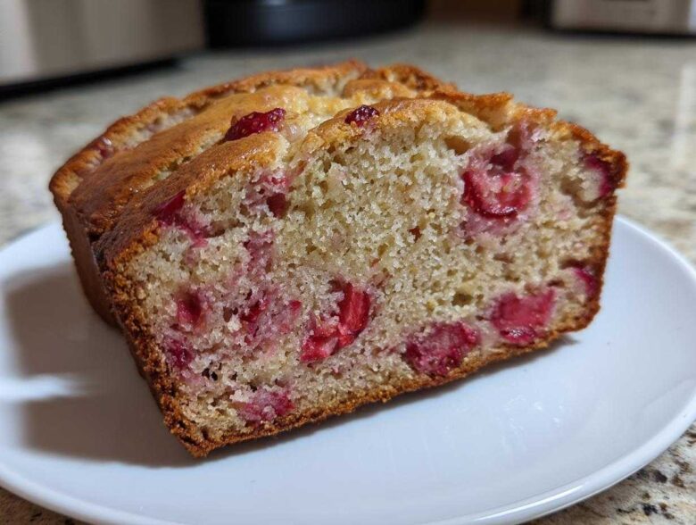 Close-up of a moist slice of Gluten-Free Strawberry Banana Bread showing bright red strawberry pieces throughout the crumb.