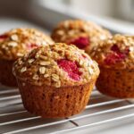 Close-up of several freshly baked Gluten-Free Strawberry Oat Muffins cooling on a wire rack, topped with oats and bright red strawberries.