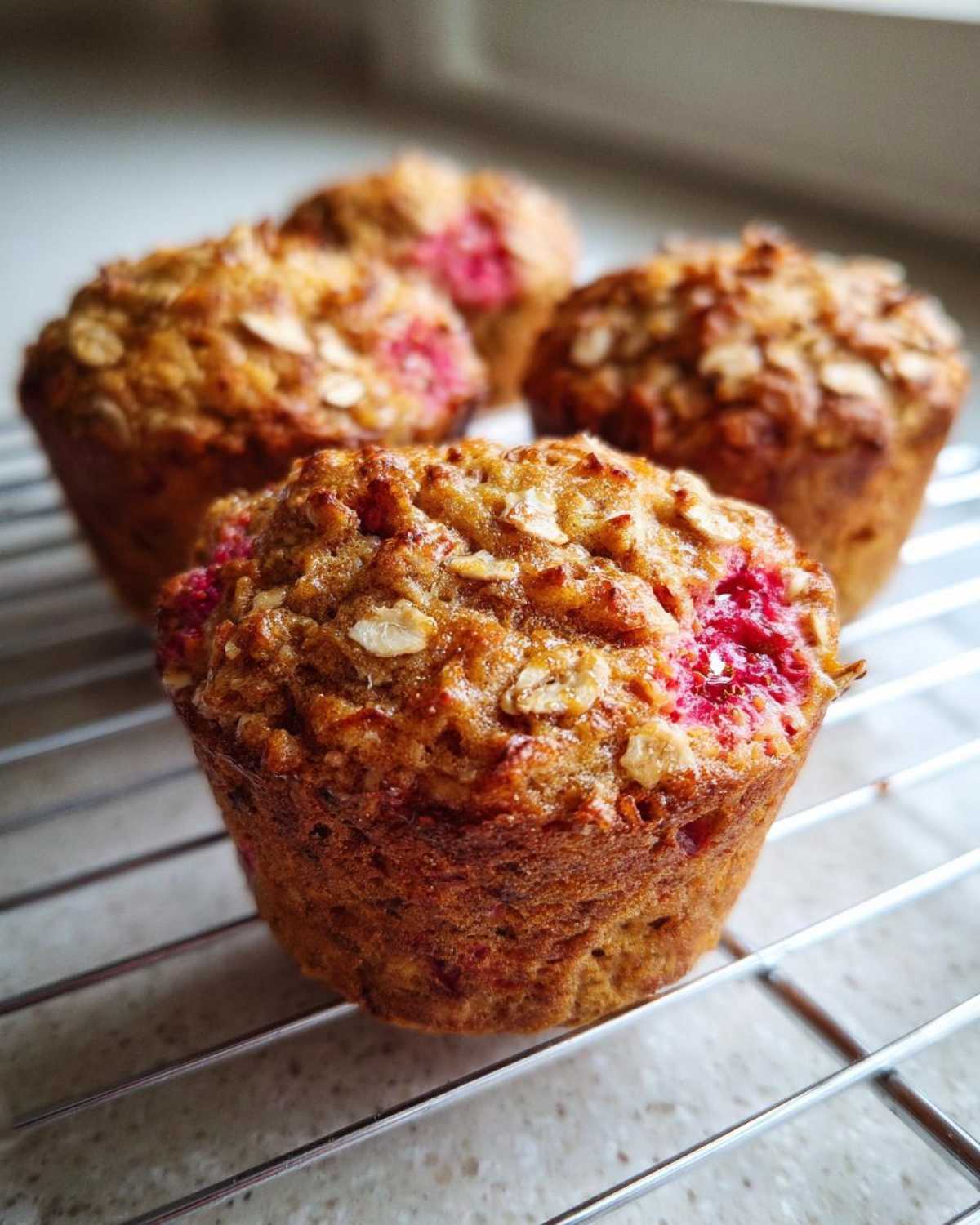 Close-up of freshly baked Gluten-Free Strawberry Oat Muffins cooling on a wire rack, showing oats and bright pink strawberry pieces.