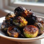 A close-up of perfectly caramelized Honey Balsamic Air Fryer Brussels Sprouts piled high in a white bowl.