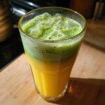 Close-up of an Iced Matcha Pineapple Refresher showing bright yellow juice topped with green, foamy matcha and ice cubes.