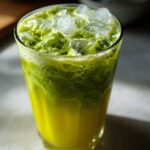 Close-up of a vibrant Iced Matcha Pineapple Refresher layered with bright yellow juice and frothy green matcha on ice.