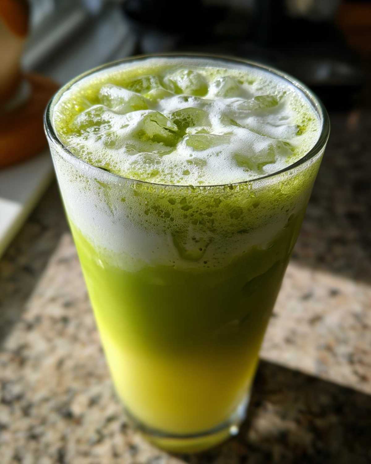 Close-up of a tall glass filled with an Iced Matcha Pineapple Refresher, showing layered yellow and green liquids with ice and foam.