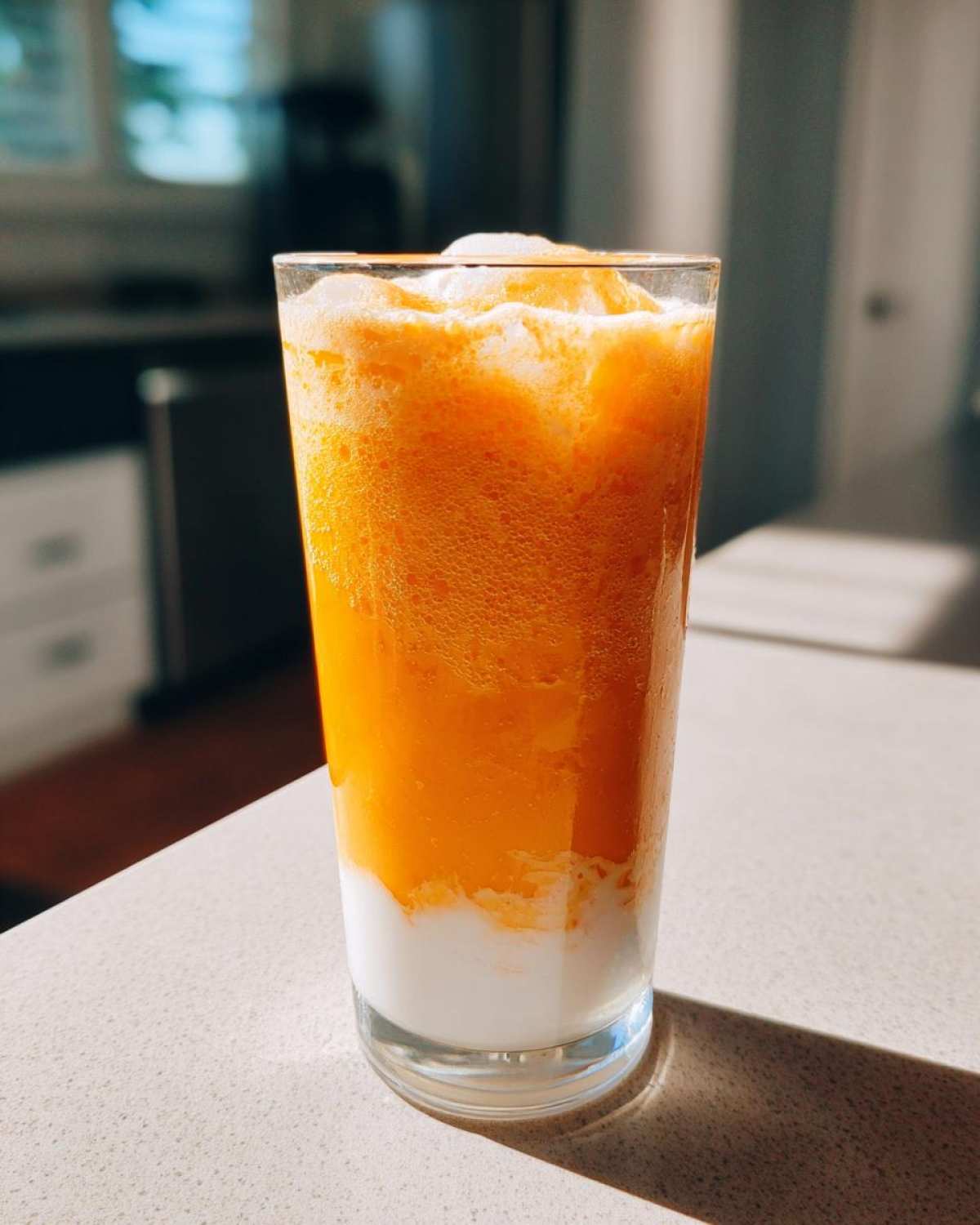 A tall glass filled with a layered Iced Orange Creamsicle Smoothie, showing bright orange frozen mixture over white milk.