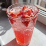 Close-up of a tall glass filled with bubbly Iced Strawberry Hibiscus Tea Lemonade and fresh strawberry slices.