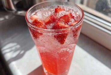 Close-up of a tall glass filled with bubbly Iced Strawberry Hibiscus Tea Lemonade and fresh strawberry slices.