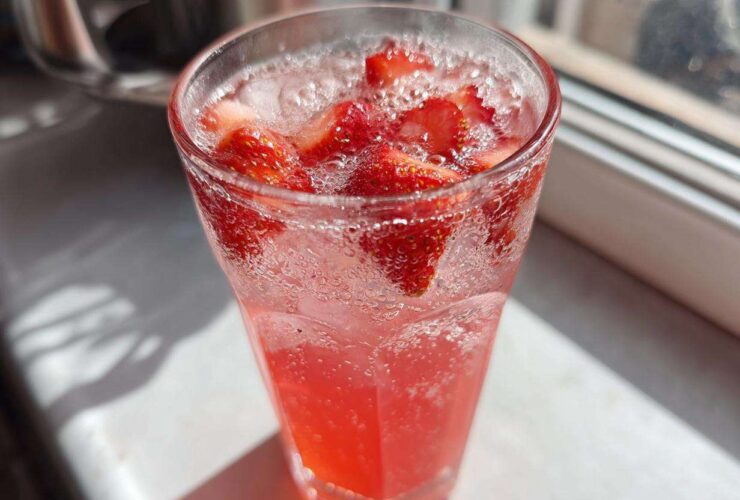Close-up of a tall glass filled with bubbly Iced Strawberry Hibiscus Tea Lemonade and fresh strawberry slices.